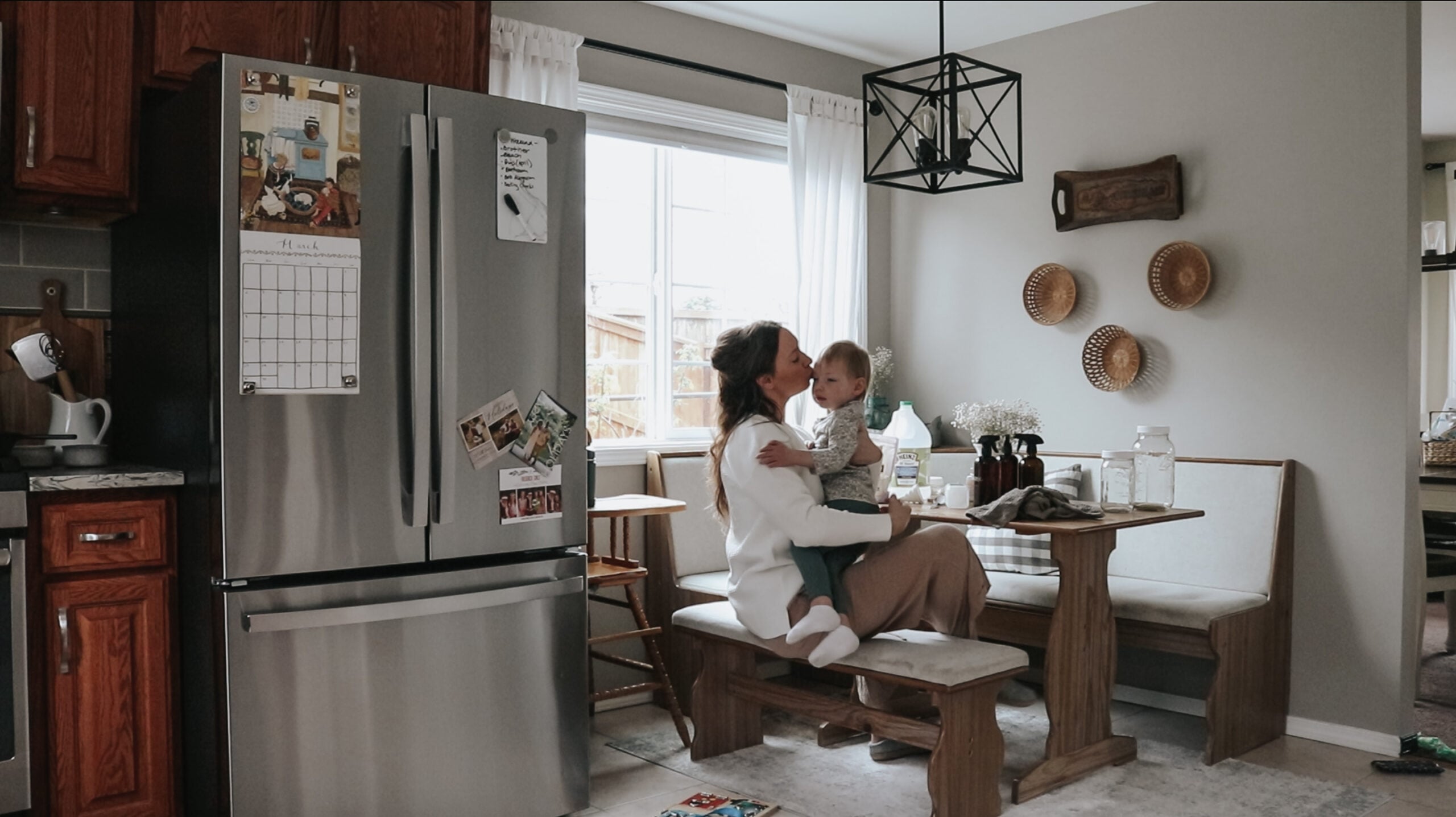 Homemaker sits at her kitchen table holding her child. She is kissing her child on the cheek.